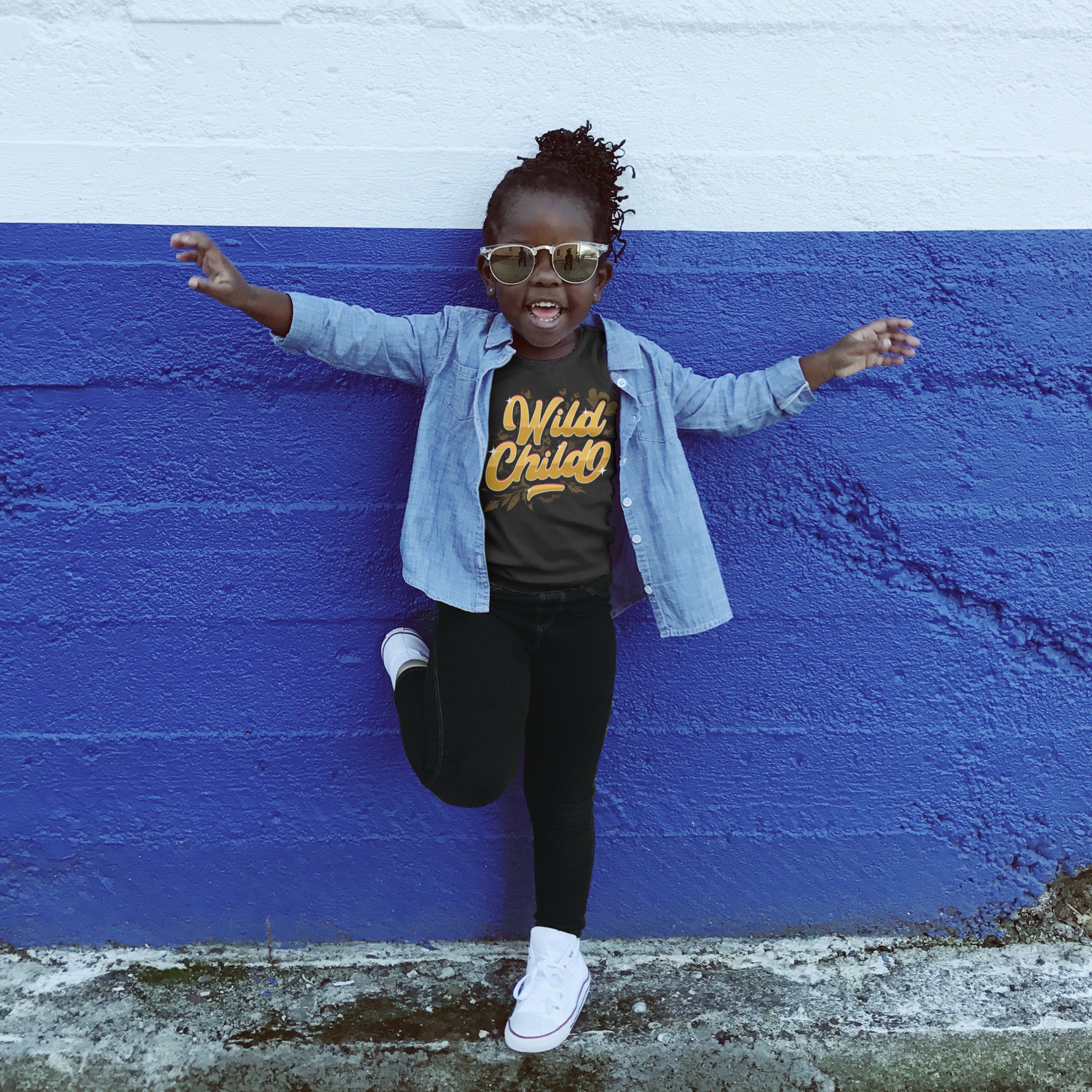 Child posing against a blue and white wall wearing sunglasses and a 'Wild Child' shirt.